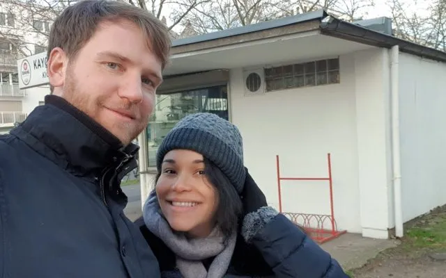 A tall man standing next to a shorter woman taking a selfie while going for a walk in the winter. Showing emotions of happiness but also tiredness as labor contractions just started and they will have a baby soon.
