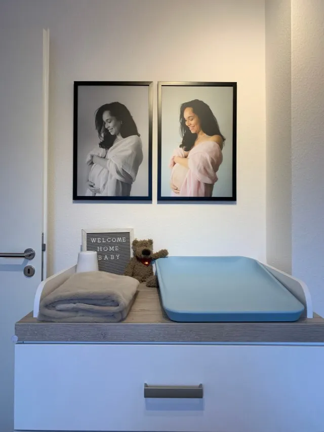 Photo of a baby changing table which includes baby accessories at the top of changing table and two photos on the wall above the changing table.
