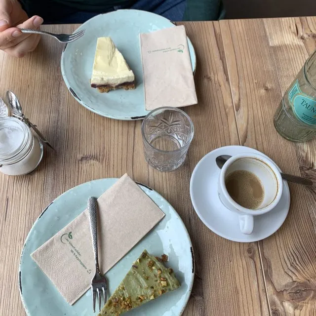 Photo of a wooden table at a cafe. On top of the table are two pieces of cake and a coffee. Signaling a husband and wife out on a date.