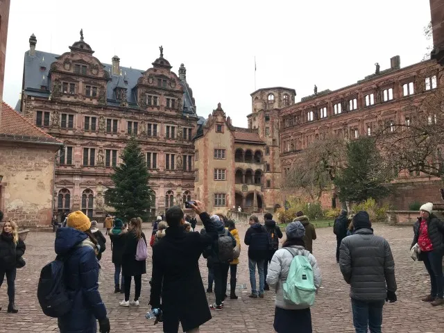 Group of tourists exploring Mannheim, Germany. The group is crowded around an old historic building while taking pictures of the site.