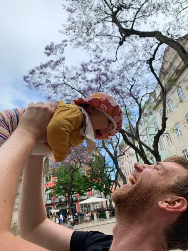 Man holding his daughter up in the air, both are laughing and enjoying the moment.