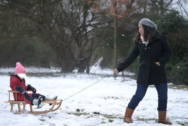 A happy mother pulling her daughter on a sleigh ride.