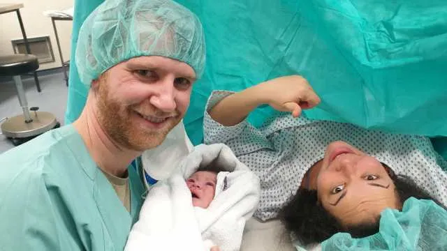 Man, woman and baby in the hospital after woman gave birth via c-section. Everyone is happy and smiling.